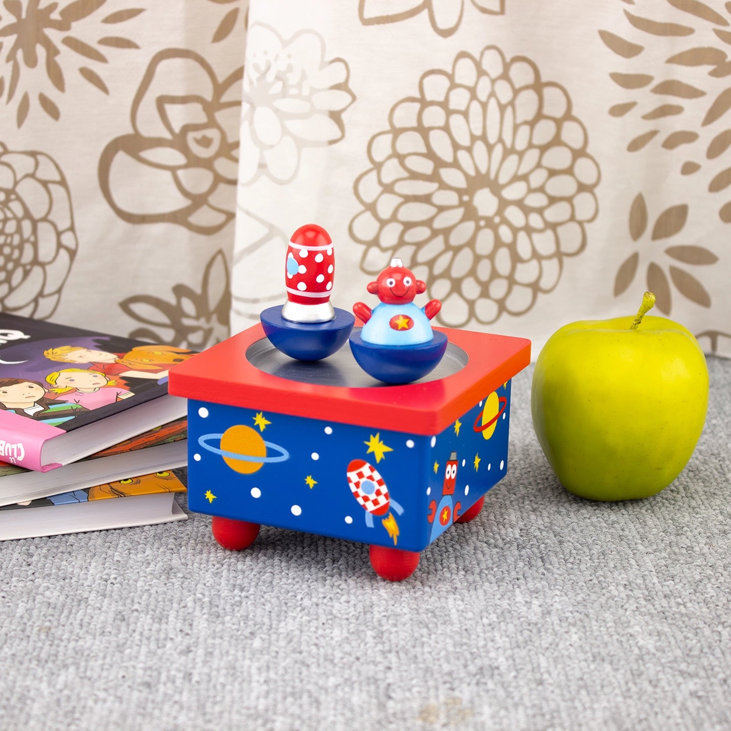 Colorful toy with space-themed design on a surface with books and an apple.